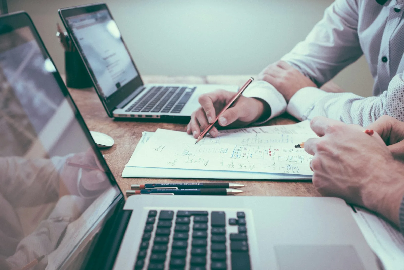 Two people working through paperwork at a desk with laptops